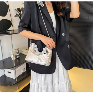 Detail of embroidered floral satin bag featuring large pearl handle and metal chain