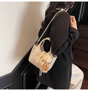 Dettaglio borsa a mano beige texture litchi con ciondolo a orsetto e chiusura dorata