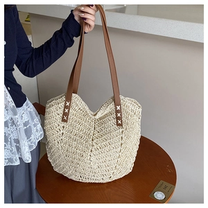 Detailed view of handmade woven straw tote with brown leather handles and cross-stitch detail