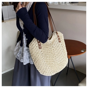 Detail of hand-woven straw tote with brown leather strap and white X-shaped stitching
