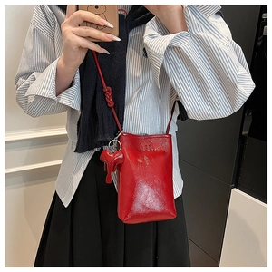 Detail of red glossy mini crossbody phone bag with embossed M logo and elephant charm