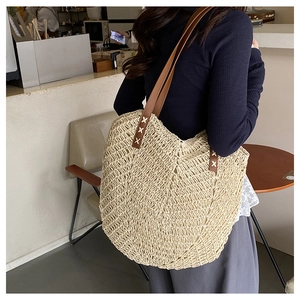 Close-up of woven straw tote bag with brown straps and detailed cross-stitch sewing