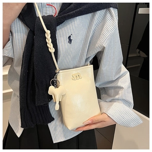 Detail of cream crossbody phone bag with m-letter logo and elephant charm accessory