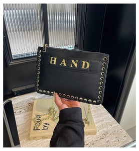Detail of black woven leather bag featuring gold HAND text and metal chain strap