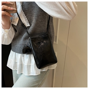 Detail of a black glossy leather crossbody phone bag with an M logo and a cute charm