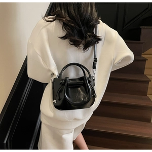 Detail der schwarzen Lack-Eimertasche mit verstellbarem Gurt zum weißen Outfit