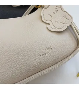 Detail of cream white litchi grain leather crescent bag with puppy charm and logo
