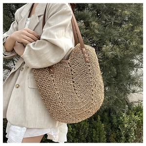 Detail of hand-woven straw tote bag with brown leather handle and reinforced stitching