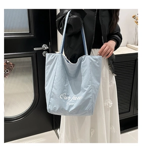 Detail of light blue tote bag with white Our fave Party lettering and long shoulder straps