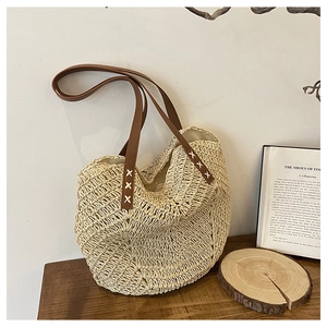 Detail of straw tote bag featuring brown leather straps and white cross-stitch embroidery