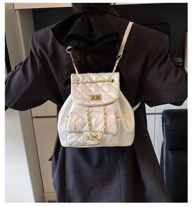 Detail of white quilted mini backpack featuring gold-tone chain straps and a twist lock