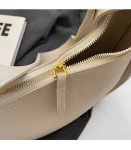 Close-up of golden zipper hardware and lychee pattern leather on beige shoulder bag