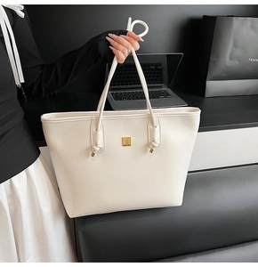 Close-up of white PU leather tote bag featuring a golden square logo and knot strap detail