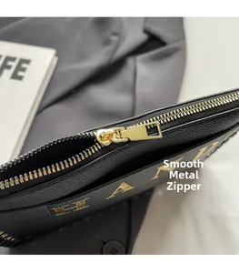 Detail of black lychee leather envelope bag with smooth golden metal zipper and foil letters
