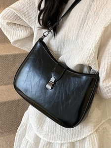 Minimalist black glossy underarm bag with metal buckle worn by model on white dress