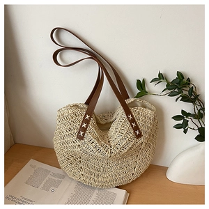 Detail of hand-woven straw tote with dark brown leather straps and white X-stitching