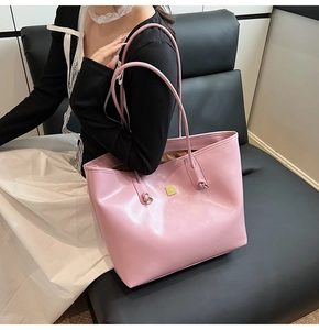 Detailed close-up of pink faux leather tote bag featuring gold square logo and knotted metal decor