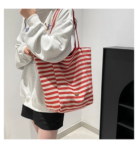 Detail of red and white striped canvas tote bag with leather logo patch and red shoulder strap
