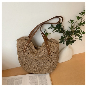 Detail of a beige woven straw tote bag featuring brown leather handles and cross-stitch accents