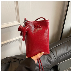 Detail of red patent leather phone bag featuring a cute elephant charm and M logo