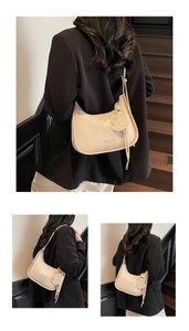 Detail showing creamy beige litchi leather crescent bag with cute bear charm on a strap