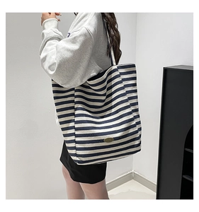 Detail of blue and white striped canvas tote bag showing handmade metal logo emblem