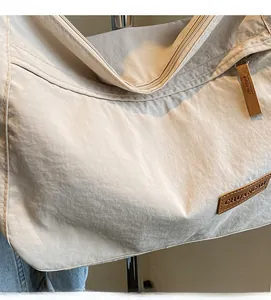 Close-up of beige nylon tote bag showing brown leather logo and wrinkled texture fabric
