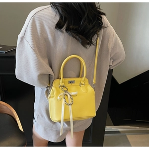 Detail of yellow cross-body bag with silver lock and white silk ribbon accessory