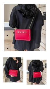 Detail of red leather envelope bag featuring gold HAND logo and metal eyelet trim