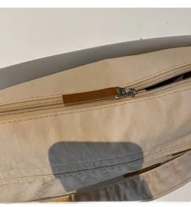 Close-up of smooth metal zipper and brown leather pull on beige nylon tote bag
