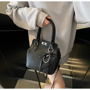 Detail of black lychee grain leather handbag featuring silver hardware and a pearl ribbon charm