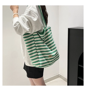Detail view of large green and white striped canvas tote bag worn over the shoulder
