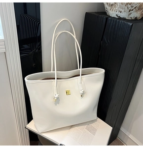 Detailed close-up of a white tote bag with golden metal logo and elegant knot handle