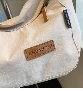 Detail of the brown leather logo patch on a beige nylon tote bag with soft texture