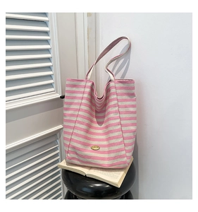 Detail of a pink and white striped canvas tote bag with a gold metal plate logo