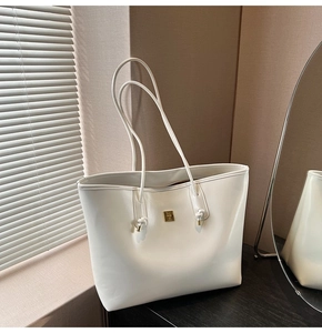 Detailed shot of white faux leather tote bag with gold hardware on a dark wooden surface