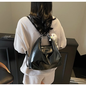 Détail d'un sac cabas noir en cuir verni brillant avec un charmant pompon blanc