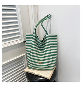 Detail of green and beige striped canvas tote bag with metal logo on a wooden chair