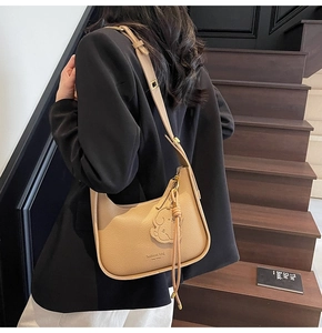 Detail of khaki crescent shoulder bag with litchi texture and cute dog charm accent