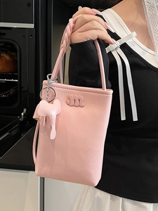Pink lychee textured crossbody bag with m-logo and elephant charm in indoor scene