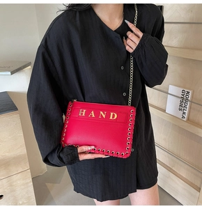 Detail of red woven envelope bag with gold HAND lettering and chain strap held by model