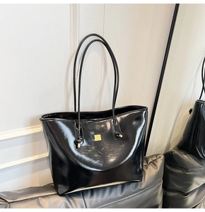 Close-up of black oil wax leather tote bag with glossy finish and gold square ornament