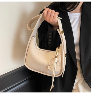 Detail of cream lychee texture leather shoulder bag with cute dog charm and logo