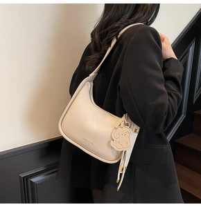 Detail of creamy white litchi pattern leather armpit bag with bear pendant and logo