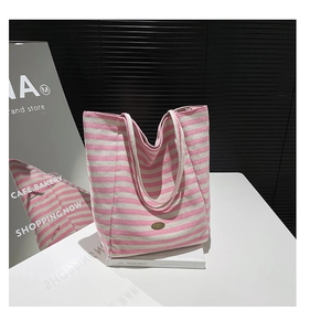 Detail of canvas tote bag with pink stripes and oval metal logo on minimalist background