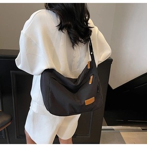 Close-up of black nylon tote bag featuring brown leather brand tag and wide shoulder strap