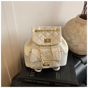 Close-up of white quilted backpack with gold chain handle and twist lock detail