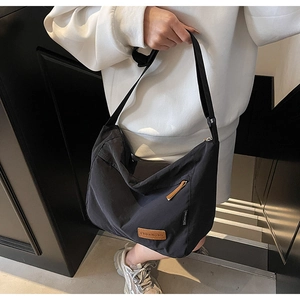 Detail of minimalist black nylon tote bag with brown leather zipper pull and side label