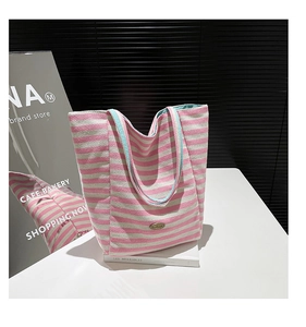 Detail of pink and white striped canvas tote bag with light blue handles and metal badge