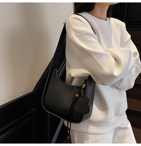 Close-up of black lychee grain leather underarm bag with a cute dog-shaped pendant charm